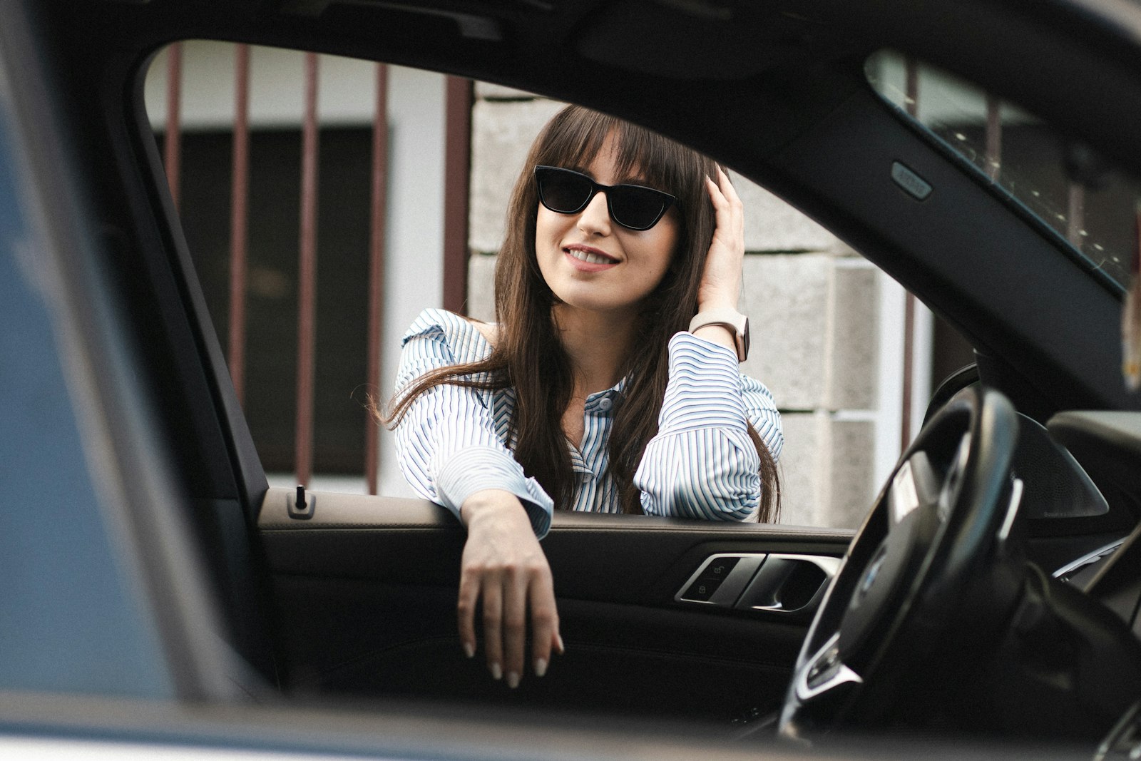 A smiling woman leaning out of her car window on a sunny day